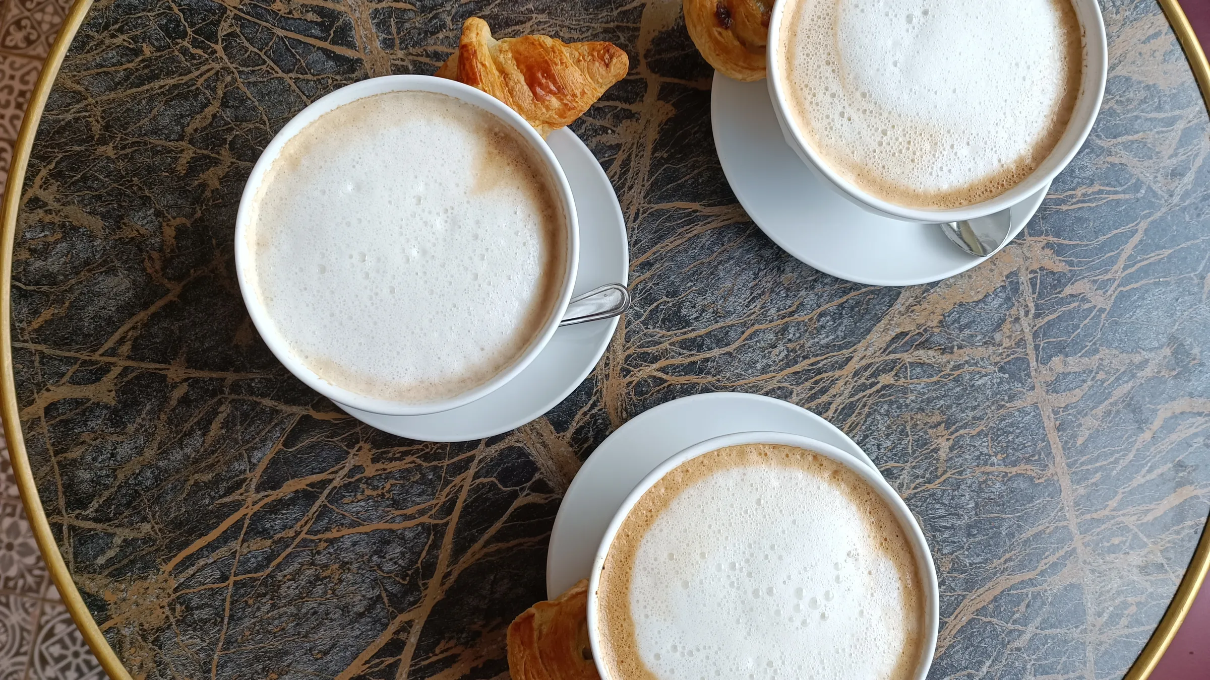 Drei Café au lait mit kleinem Gebäck auf einem Marmortisch