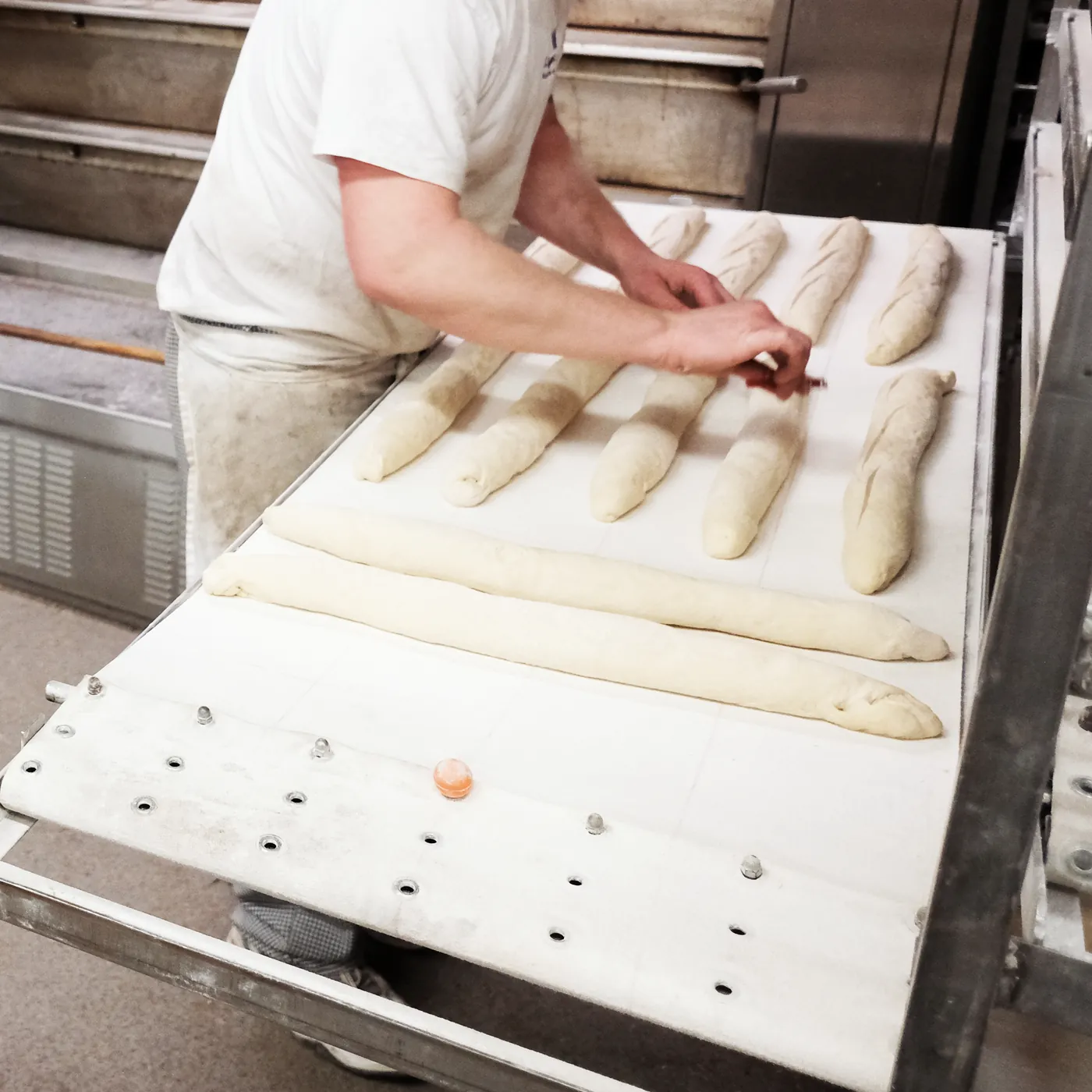 Bäcker schneidet am Ofen von Hand Baguettes ein