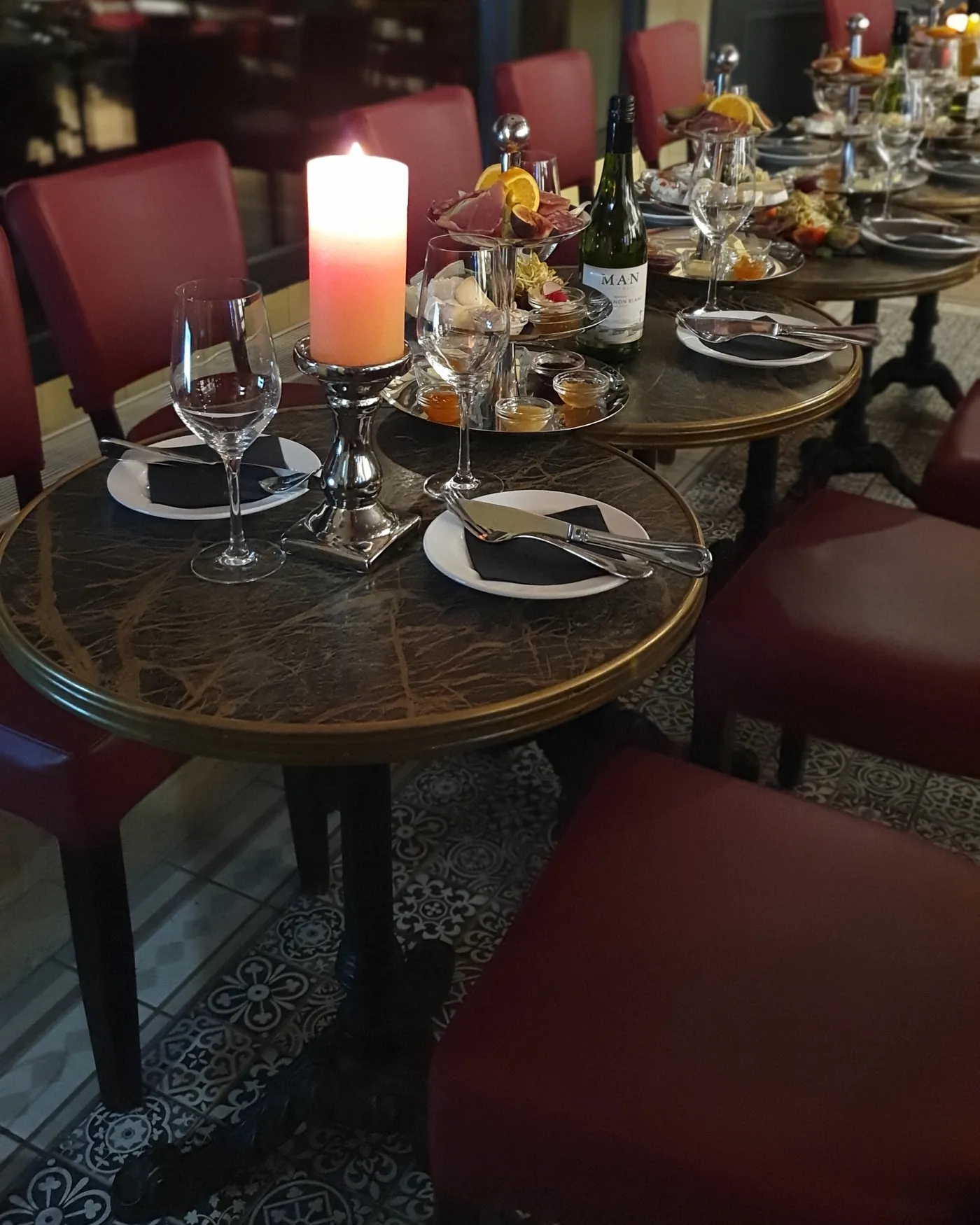 Gedeckter Marmortisch mit Kerze und Etagere, dahinter rote Stühle