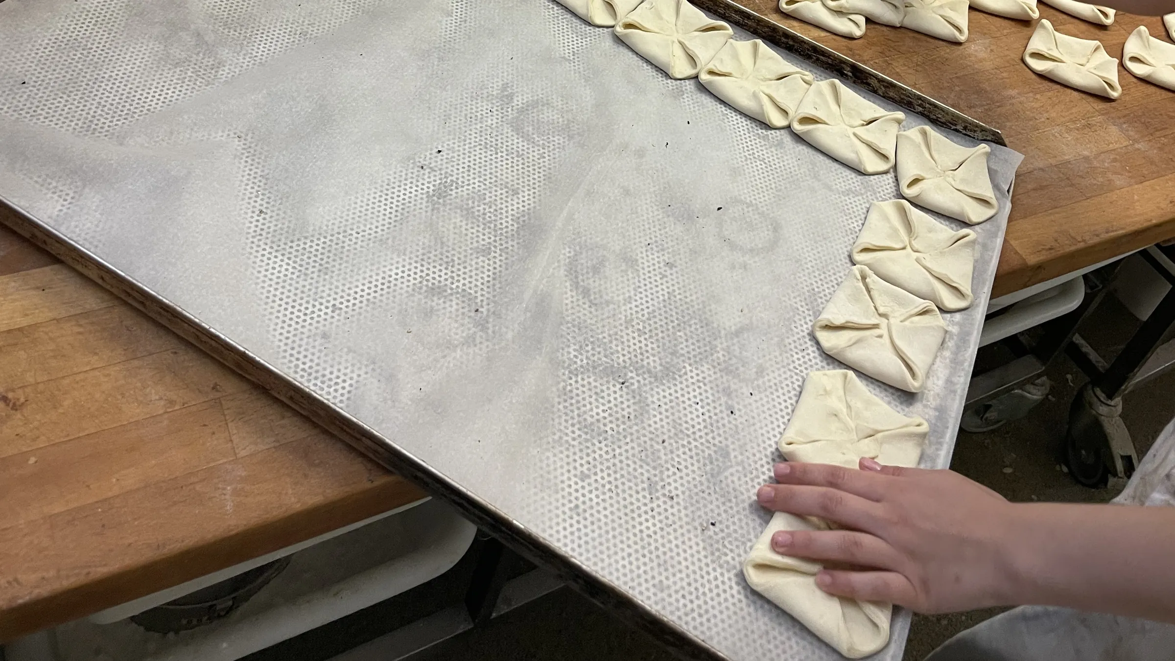 Hände formen Teigstücke auf einem Blech in der Backstube