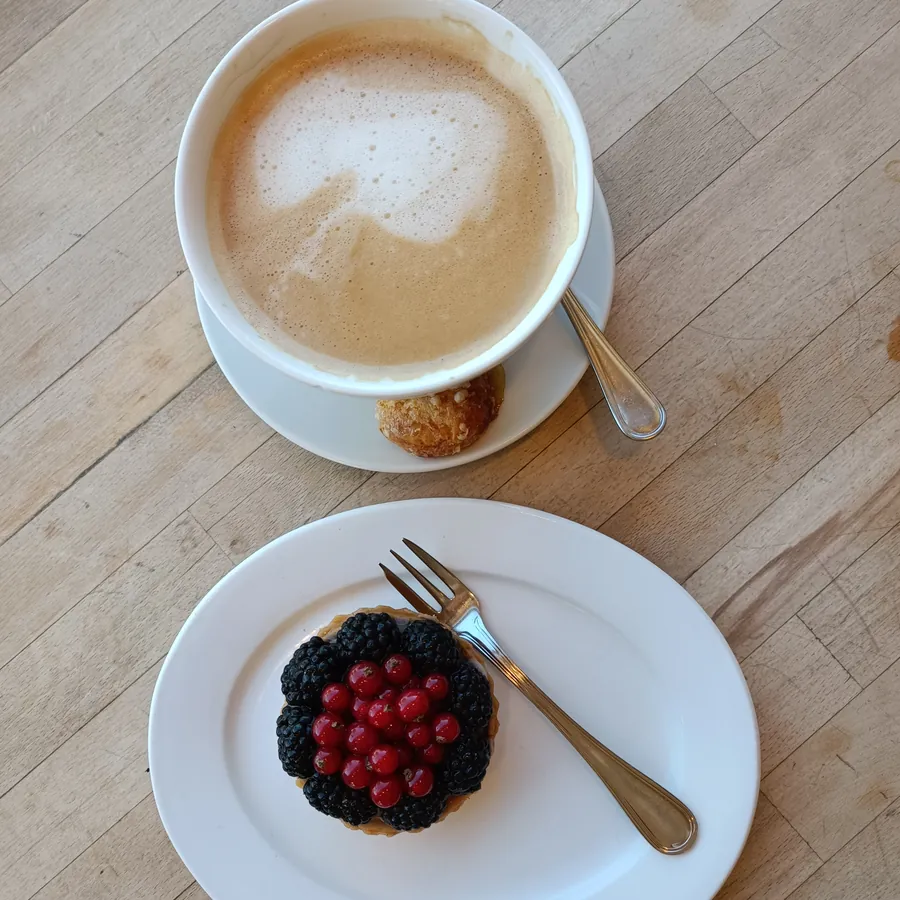 Milchkaffee und eine Beerentartelette von oben auf dem Holztresen