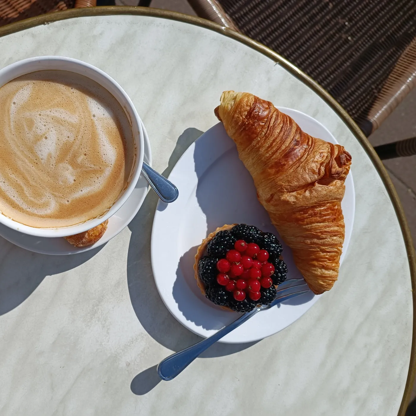Croissant und Beerentartelette neben einem Milchkaffee auf dem Marmortisch